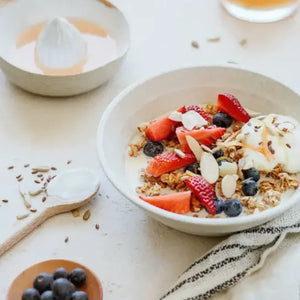 Juice next to a bowl filled with strawberries, blueberries, apple, seeds and muesli as suggested as a recipe idea for a healthy snack