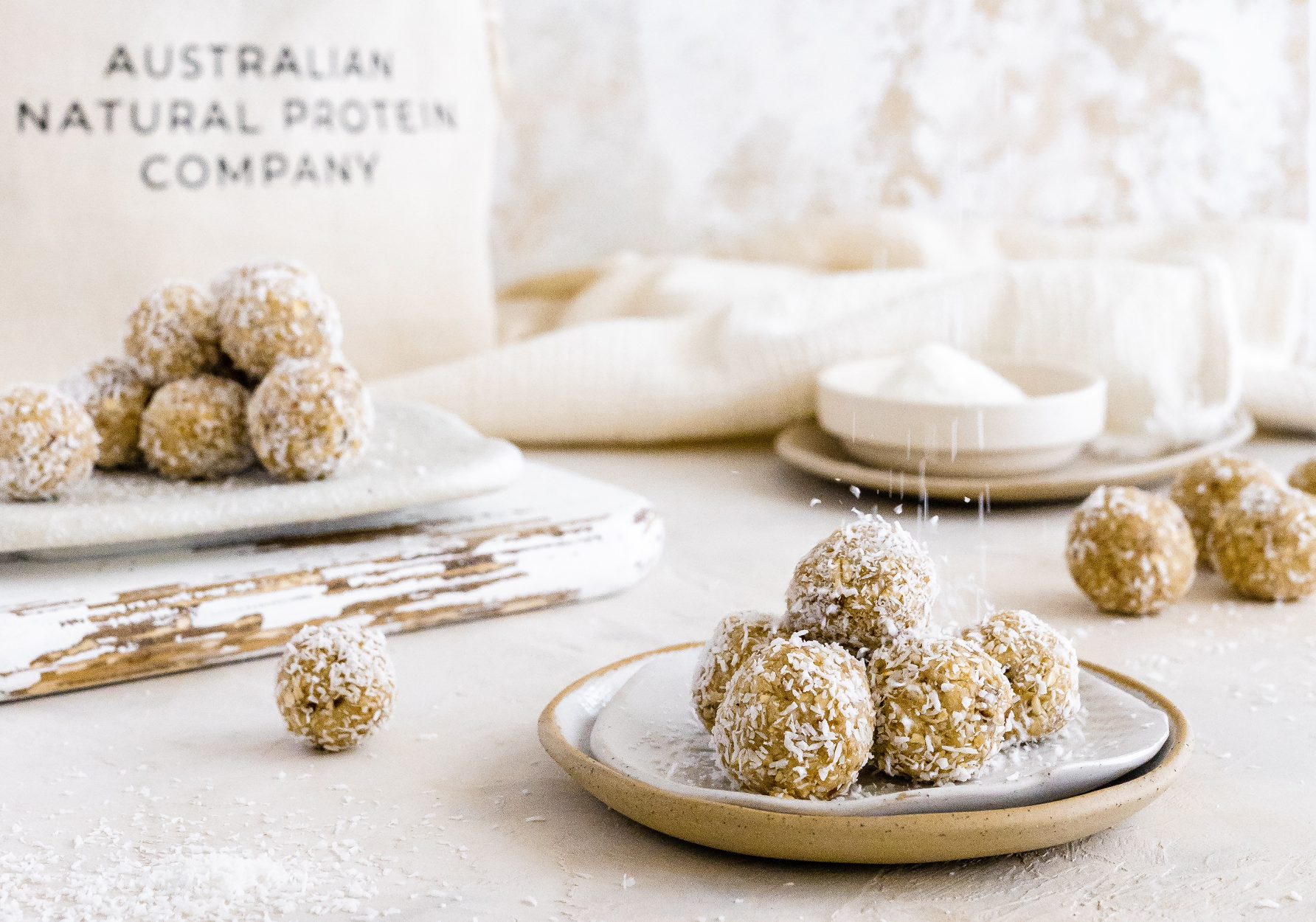 Pictured are freshly made Vanilla Bean Protein bliss balls on a plate with Australian Natural Protein Company Package of Organic Vanilla Bean Protein Whey Powder in the background